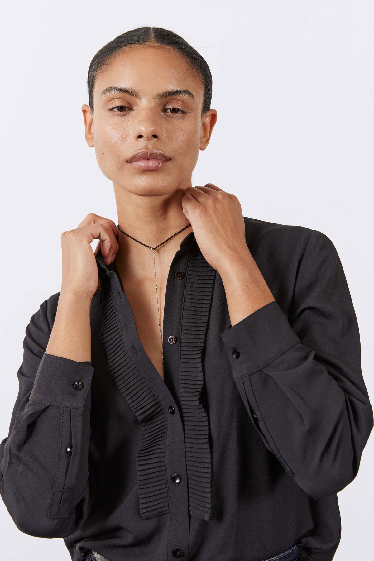 Black blouse with point collar, ribbed front placket, and buttoned cuffs