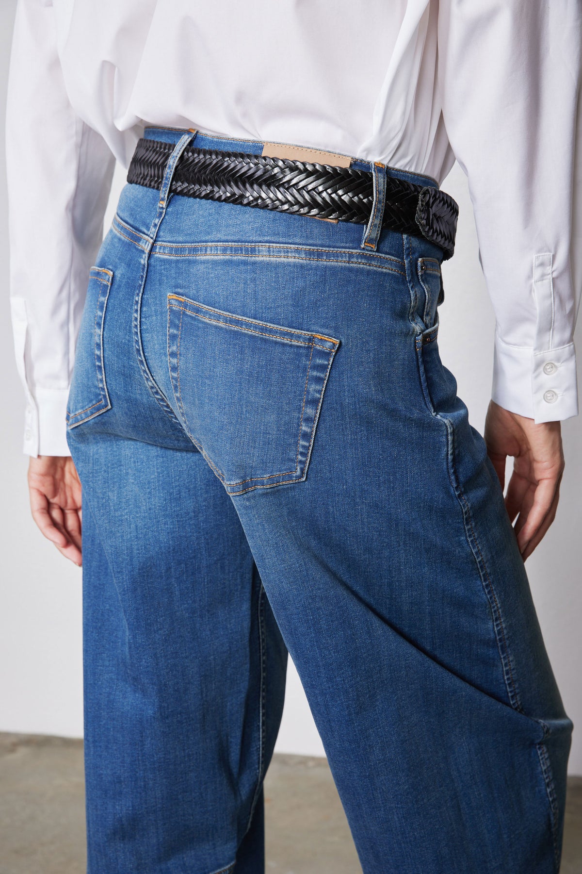 Indigo barrel-leg jeans close-up of waistband, braided belt, and hip pocket