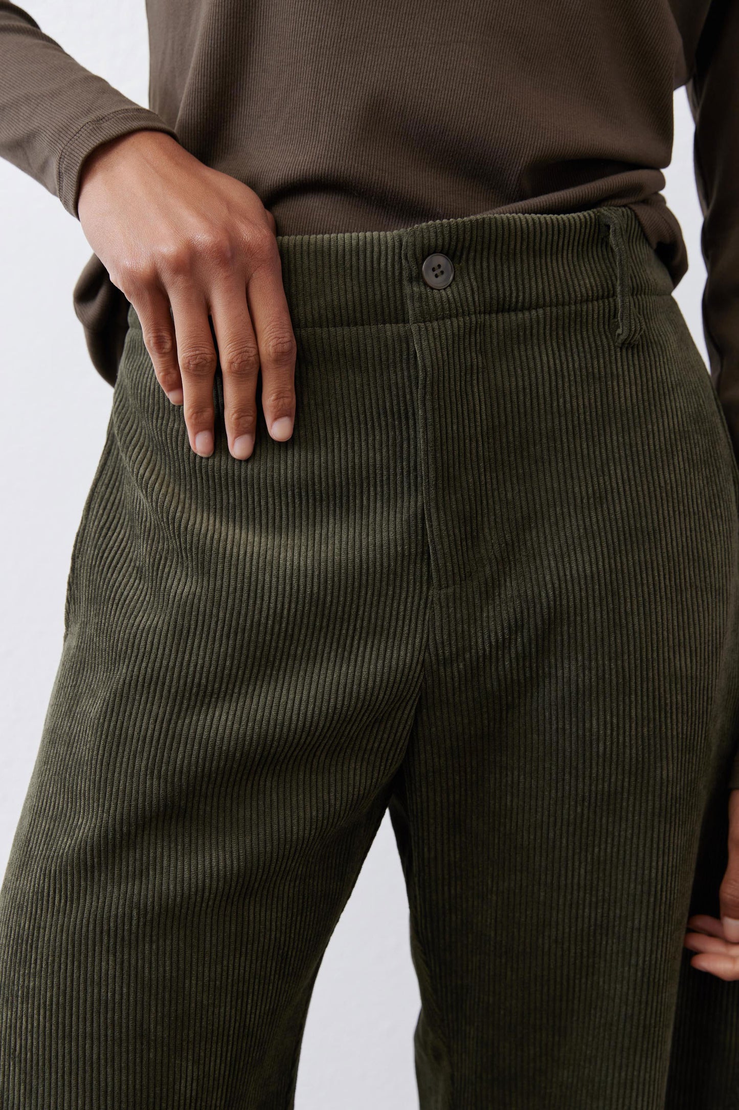 Dark green corduroy barrel pants close-up: buttoned waistband and textured fabric