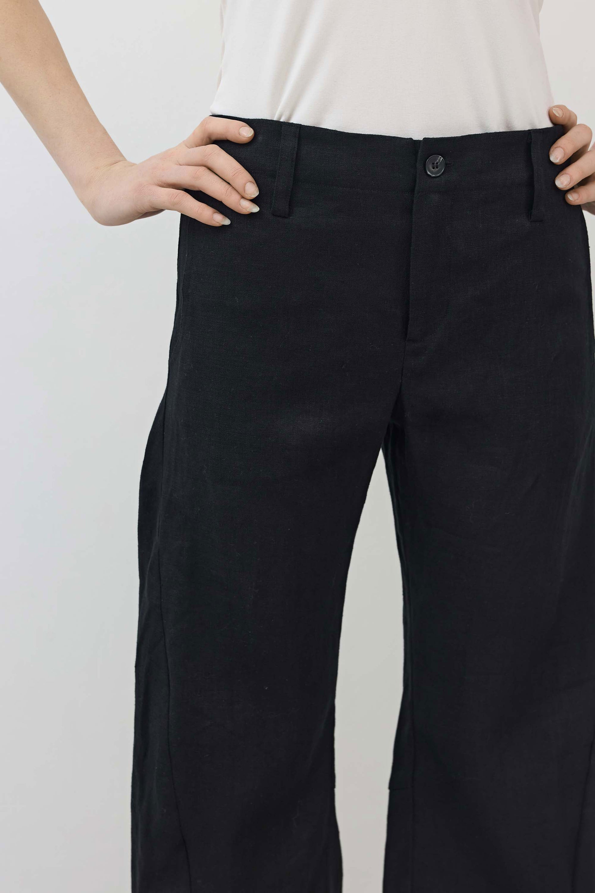 Black linen pants close-up: button waist, smooth front, relaxed drape and tapered legs