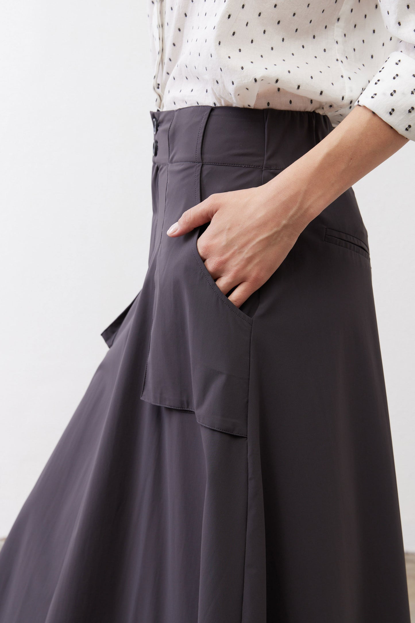 Graphite utility skirt pocket flap detail with stitched front seams and paneling.
