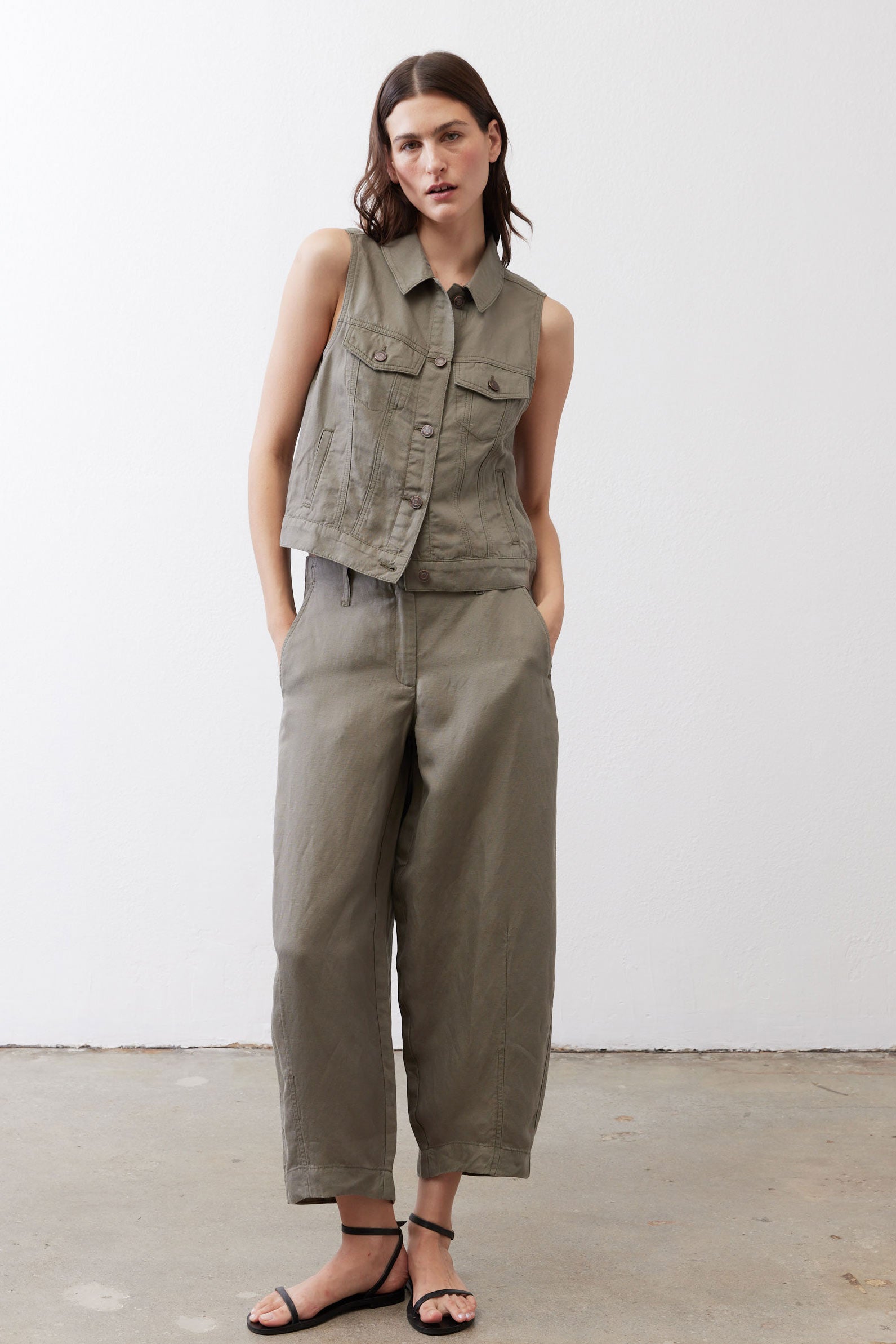 Olive green cropped task vest with button front and two chest pockets, model standing