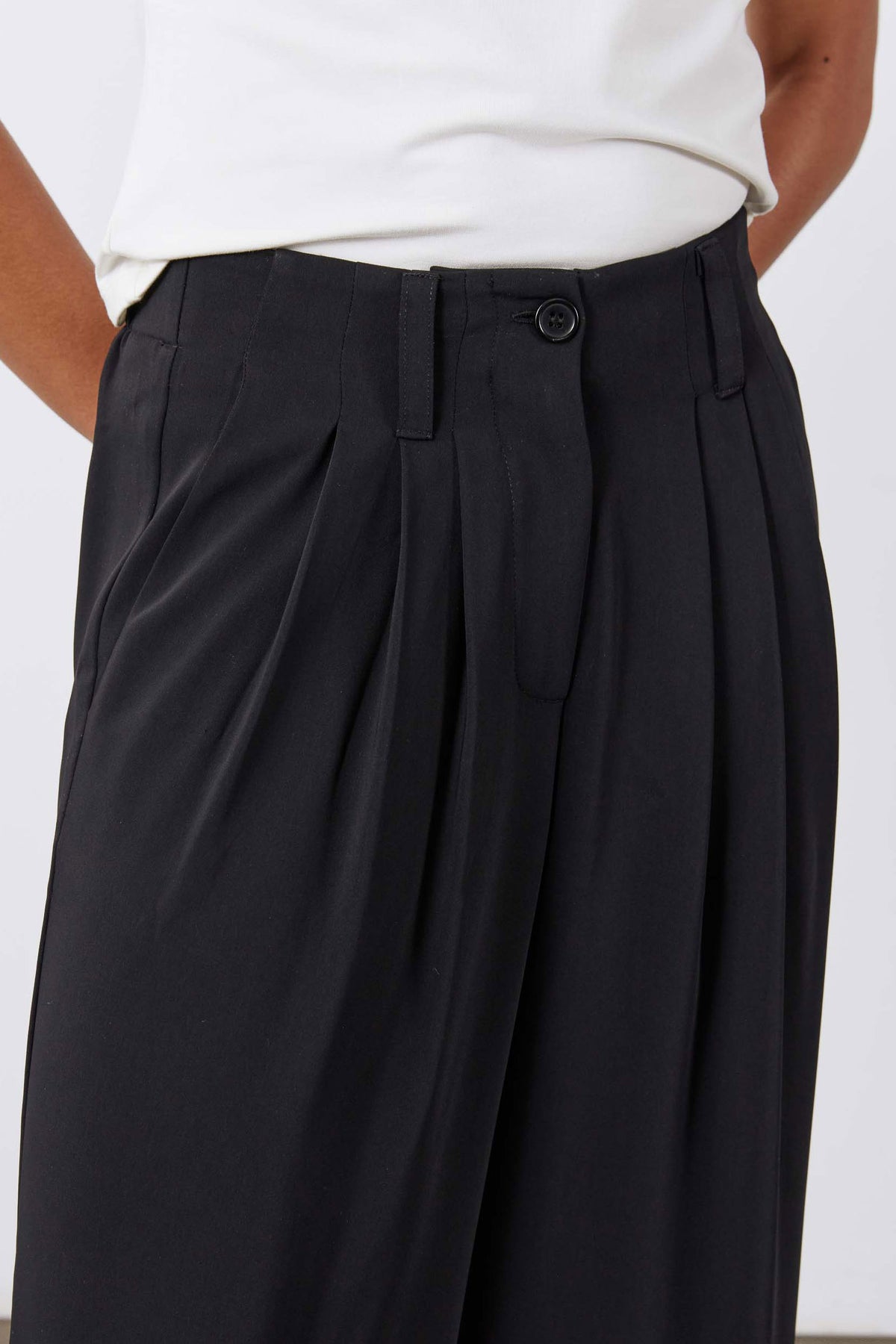 Black pleated trousers with buttoned waistband, belt loops, and deep front pleats.