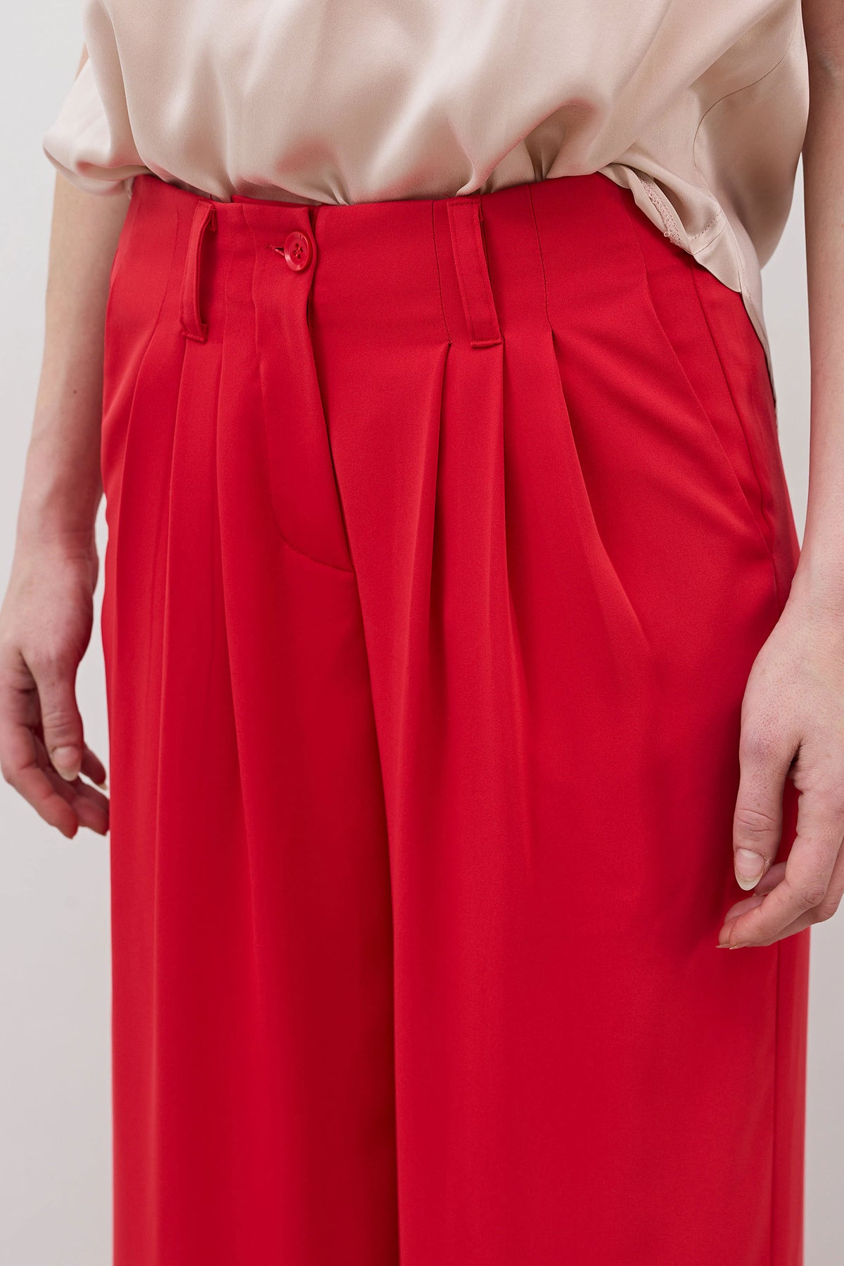 Tomato red wide-leg trousers close-up with pleats, button waistband, and belt loops