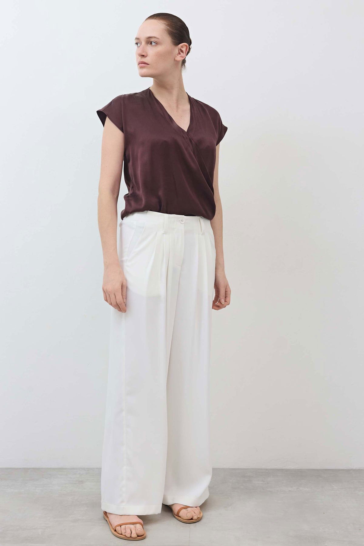Wrap silk top with V-neck and short sleeves in deep fudge brown, worn with white pants.