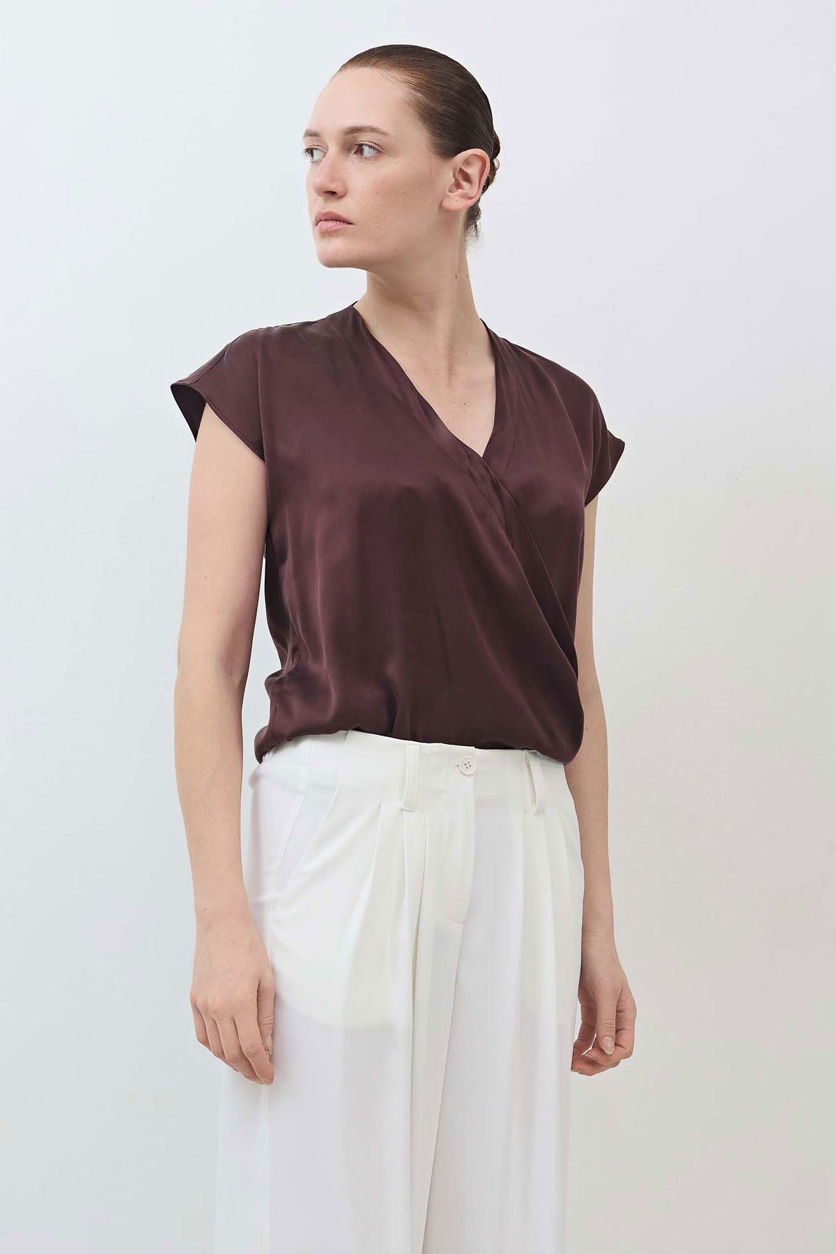Fudge brown wrap silk top with V-neck and cap sleeves, draped front; model standing sideways.